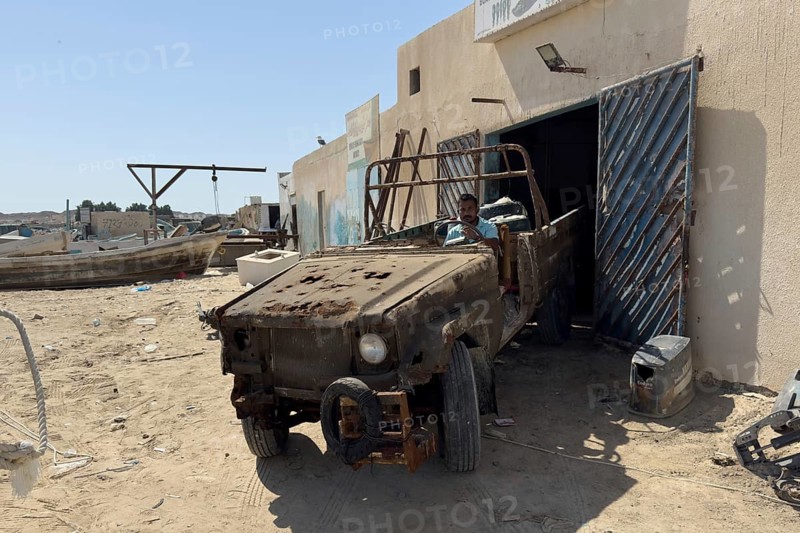Rusty and almost broken car in front of garage or workshop, Oman