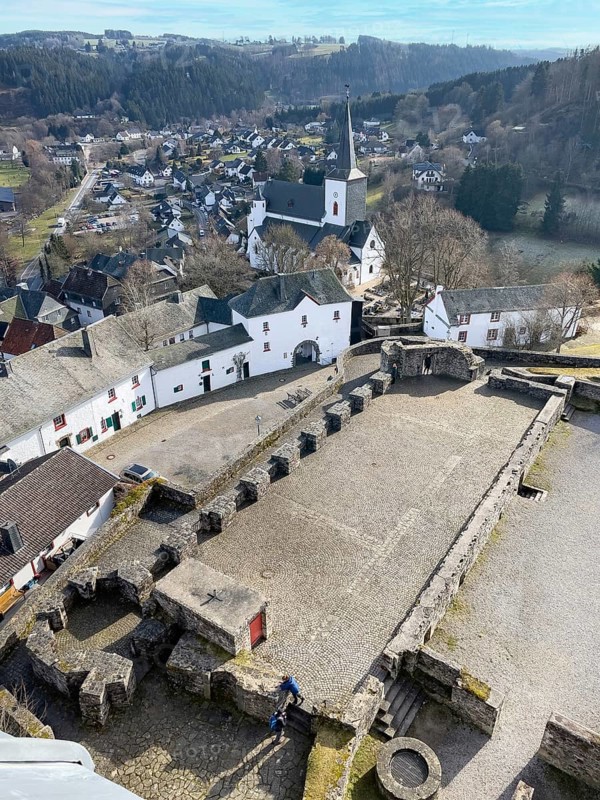 View of preserved keep made of quarry masonry castle tower on castle ruins Burghof restored preserved foundations and building remains of medieval Höhenburg Reifferscheid Castle Excursion destination in Eifel, center left preserved old buildings of still inhabited historic Burgbering Reifferscheid, Hellenthal, Euskirchen district, North Rhine-Westphalia, Germany