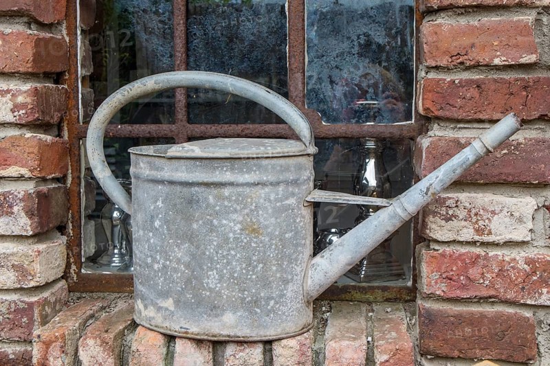 Old metal watering can on a brick window sill in front of a rusted lattice window, North Rhine-Westphalia, Germany