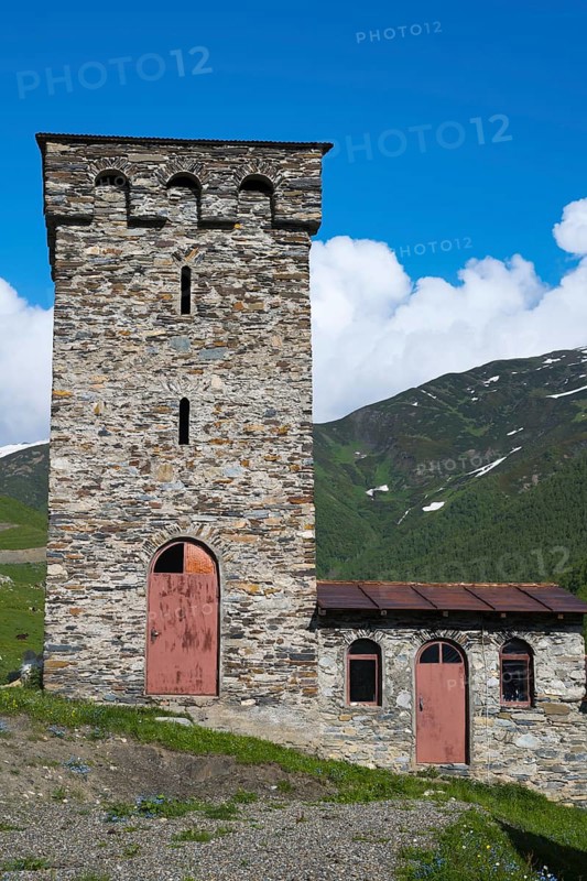 Old stone tower and small building against a mountain backdrop under a deep blue sky, defensive towers, Ushguli, Upper Svaneti, Svaneti, Georgia