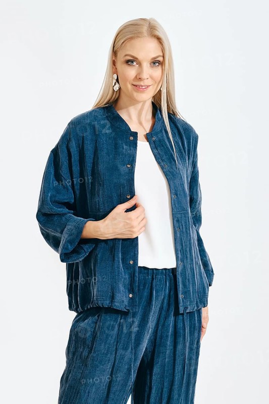 A woman stands in a studio wearing a blue outfit. She poses confidently with a smile. The environment is bright with a plain background. Her style shows a modern approach to casual fashion