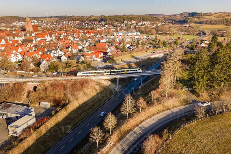Train crosses a bridge in a town with red roofs and surrounding forest, test run on the new Hermann-Hesse railway with Siemens Mireo Plus B trains, Calw, Germany