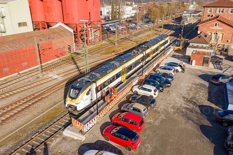 Train at train station next to red buildings with parked cars and people working in orange vests, test run on the new Hermann Hesse railway with Siemens Mireo Plus B trains, Calw, Germany