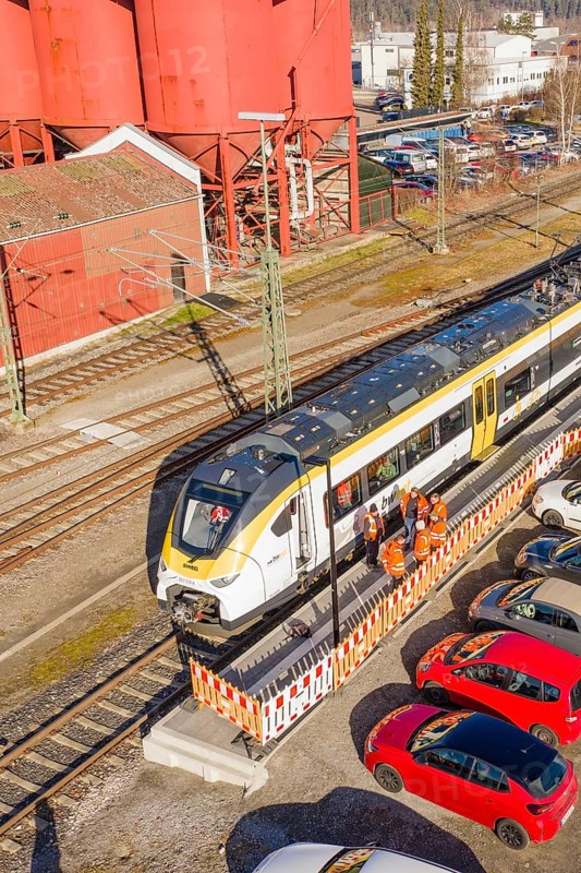 Close-up of a train at a station surrounded by industrial buildings, cars and several workers, test run on the new Hermann Hesse railway with Siemens Mireo Plus B trains, Calw, Germany