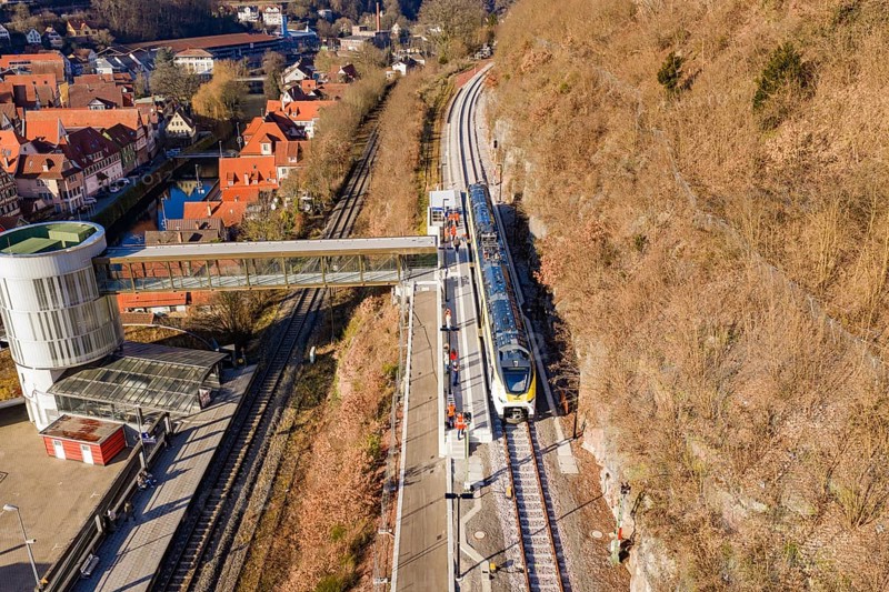Train goes under bridge surrounded by green vegetation and urban structures, test run on the new Hermann-Hesse railway with Siemens Mireo Plus B trains, Calw, Germany