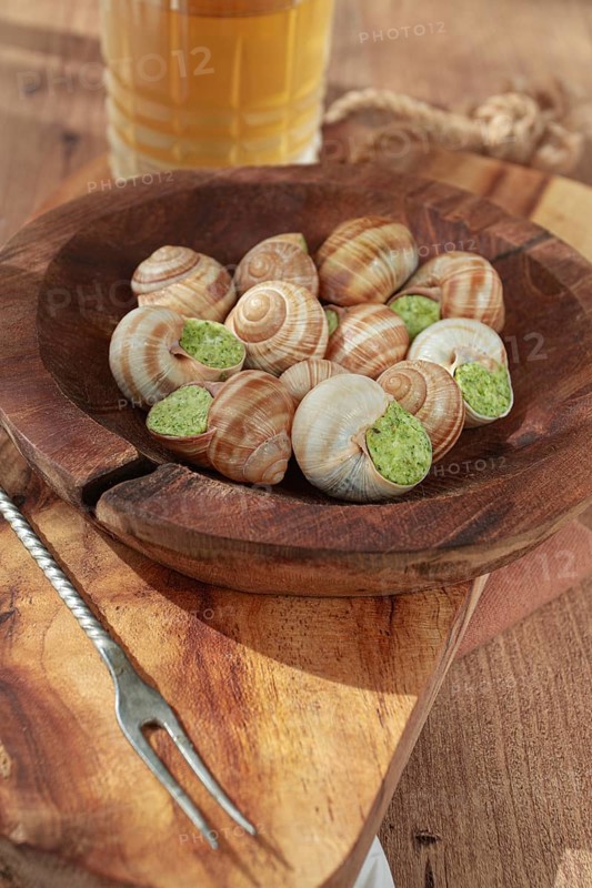 Snails cooked with herb oil on a wooden plate, served with white wine, natural light, no people
