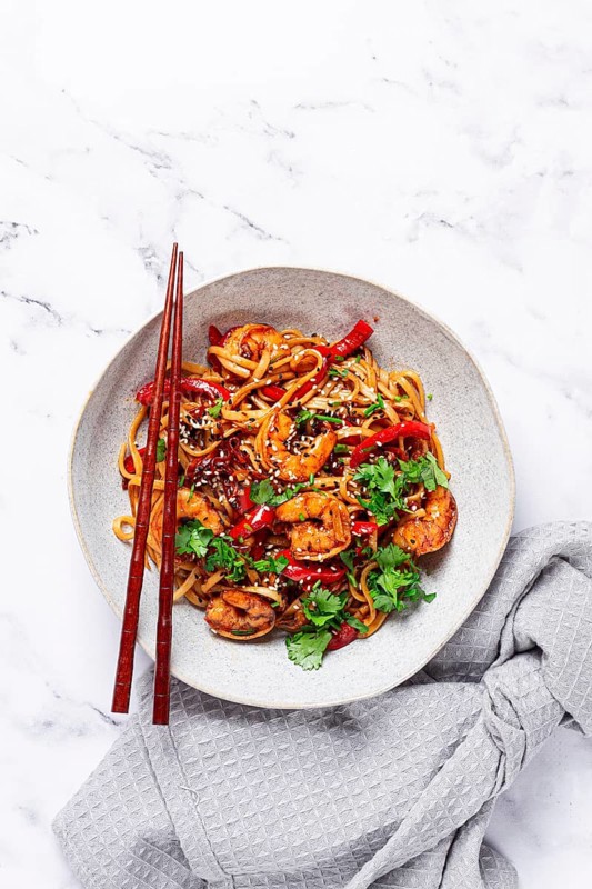 Udon noodles, shrimp with vegetables and fresh herbs, in a bowl with chopsticks, light background, homemade, no people