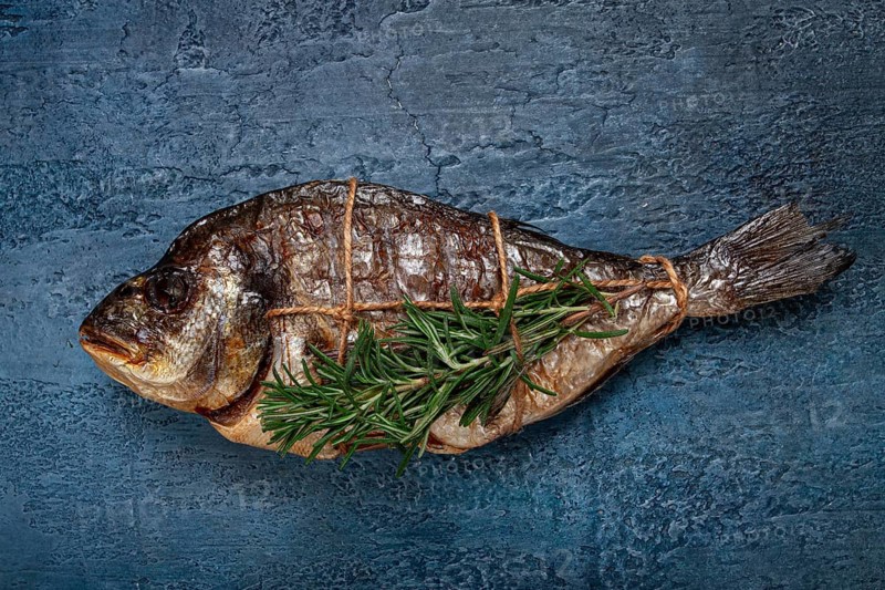 Dorado fish, hot smoked, with a sprig of rosemary, tied with a rope, on a blue background, top view, smoked fish, close-up, no people