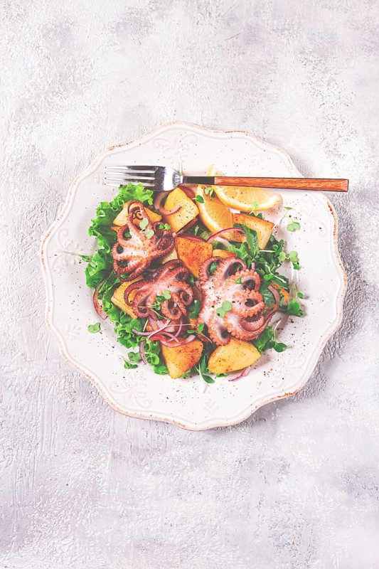 Grilled octopus with baked potatoes and fresh herbs, on a decorative light plate, homemade, no people