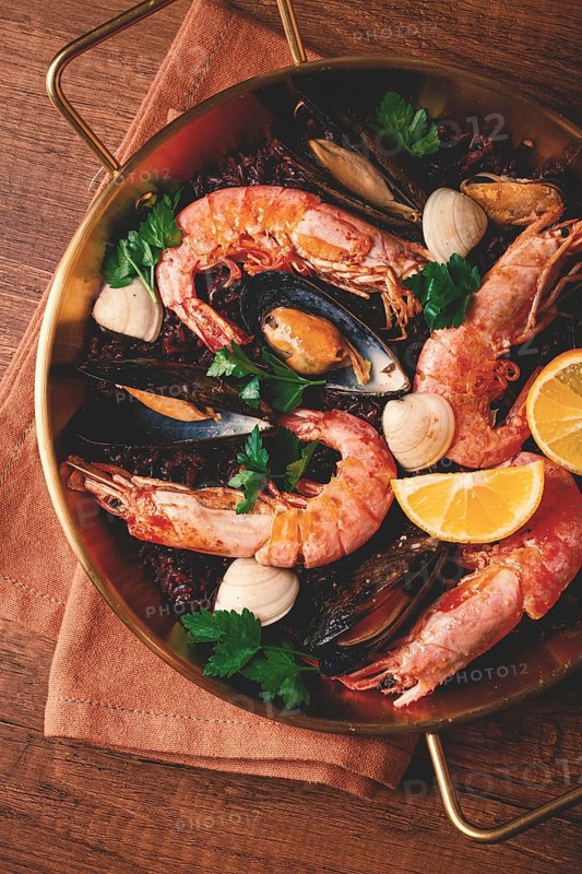 Seafood and black rice paella, in a frying pan, homemade, on a wooden table, no people