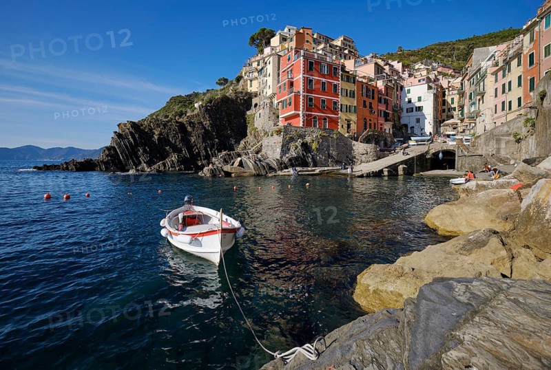 White boat, colorful houses under blue sky, view of the fishing village of Riomaggiore, port, Cinque Terre, La Spezia province, Liguria, Italy