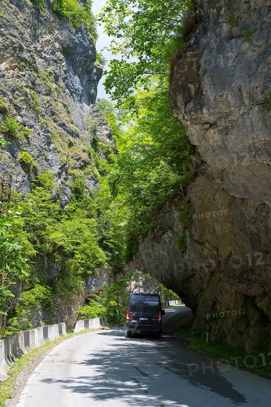 A black van passes a narrow road under a natural rock arch, camper, motorhome in a gorge on the Lajanuri River near Achara, Racha-Lechkhumi region and Lower Svaneti, Georgia