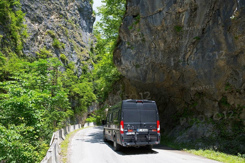 A black van drives through a narrow gorge surrounded by high rock walls and green vegetation, camper, motorhome in a gorge on the Lajanuri river near Achara, Racha-Lechkhumi region and Lower Svaneti, Georgia