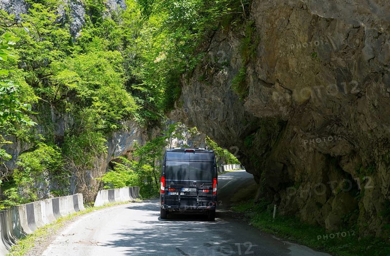 A black van drives on a narrow mountain road surrounded by lush greenery, camper, motorhome in a gorge on the Lajanuri river near Achara, Racha-Lechkhumi region and Lower Svaneti, Georgia
