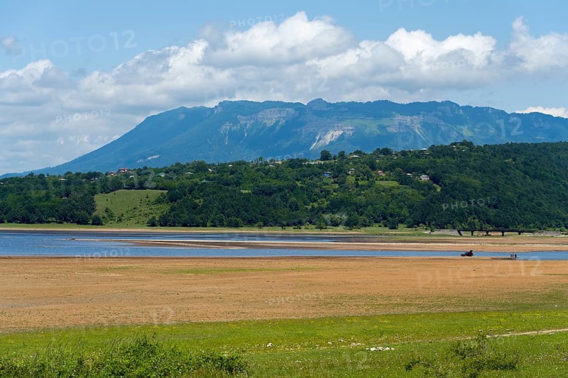 Idyllic landscape with lake, green shore and mountains in the background under a cloudy sky, Tqibuli Reservoir, Imereti Region, Georgia