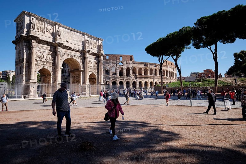 Tourists in front of the Colosseum and Arch of Constantine on a sunny day surrounded by trees, Rome, Lazio, Italy