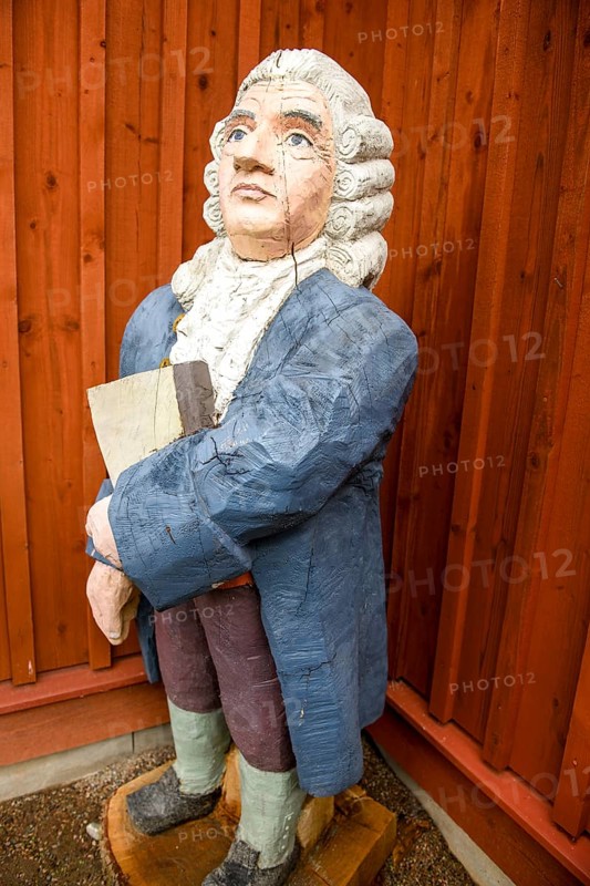 Wooden statue of botanist and founder of the binary nomenclature Carl von Linné with white hair and blue jacket in front of a wooden wall, Linnés Råshult, Älmhult, Kronobergs län, Småland, Sweden