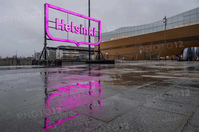 Large pink glowing city logo of Helsinki, in front of Oodi Central Library and Cultural Center, reflected on wet ground, Helsinki, Finland