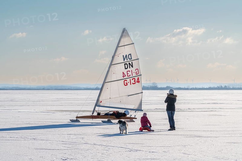 Family with dog watching sailboat on frozen Dümmer See, Lembruch, Diepholz district, Lower Saxony, Germany