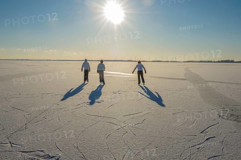 Three young woman skate on frozen Dümmer Lake under low sun, Lembruch, Lower Saxony, Germany