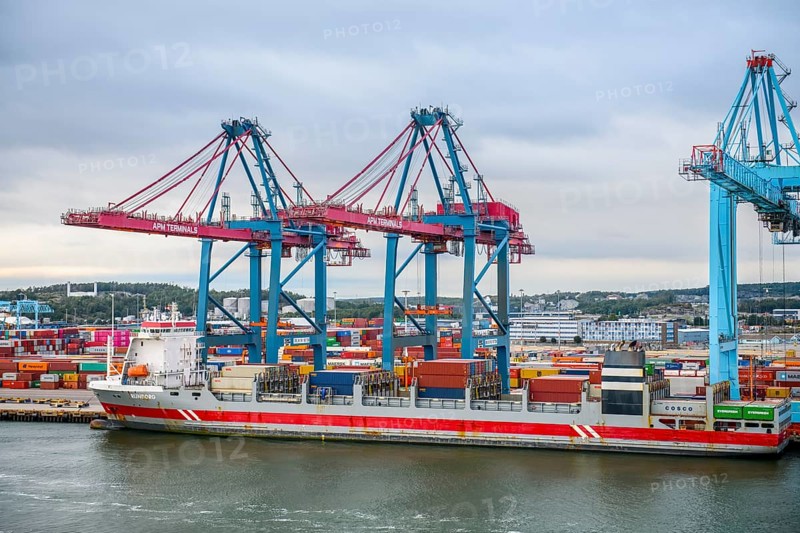 Large port with several blue and red cranes and container ships under cloudy sky, Gothenburg, Västra Götalands län, Sweden