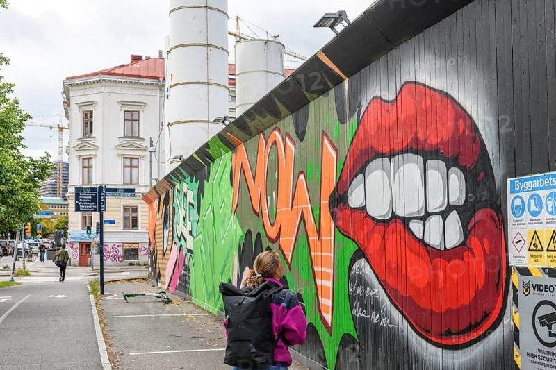 Colourful graffiti on an urban street scene with eye-catching lip motifs is viewed by a young woman, colorful mural street art, Gothenburg, Västra Götalands län, Sweden