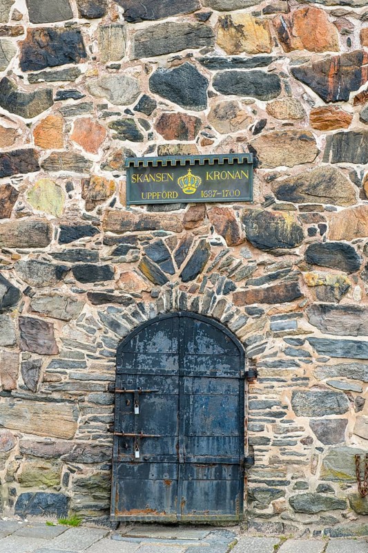 Historic stone wall with a metal door and a sign about Skansen Kronan, detail of an old stone wall in Gothenburg's Skansen Kronan fortress with historic signs, rustic masonry, Gothenburg, Västra Götalands län, Sweden