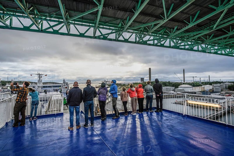 Group of people on a ship deck looking at the harbor crossing under the Älvsborgsbron suspension bridge under a cloudy sky on a ferry boat, Stena Line Gothenburg-Kiel, Gothenburg, Västra Götalands län, Sweden