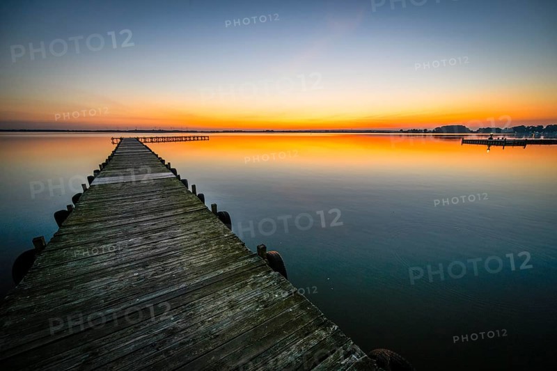 Wooden walkway leads into quiet Dümmer Lake at bright sunset, Lembruch, Dümmer See, Lower Saxony, Germany