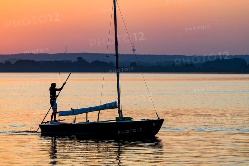 Sailing boat with person on calm Dümmer See brought into the harbor with a long stake at sunset, silhouette against orange sky, Lembruch, Dümmer See, Lower Saxony, Germany