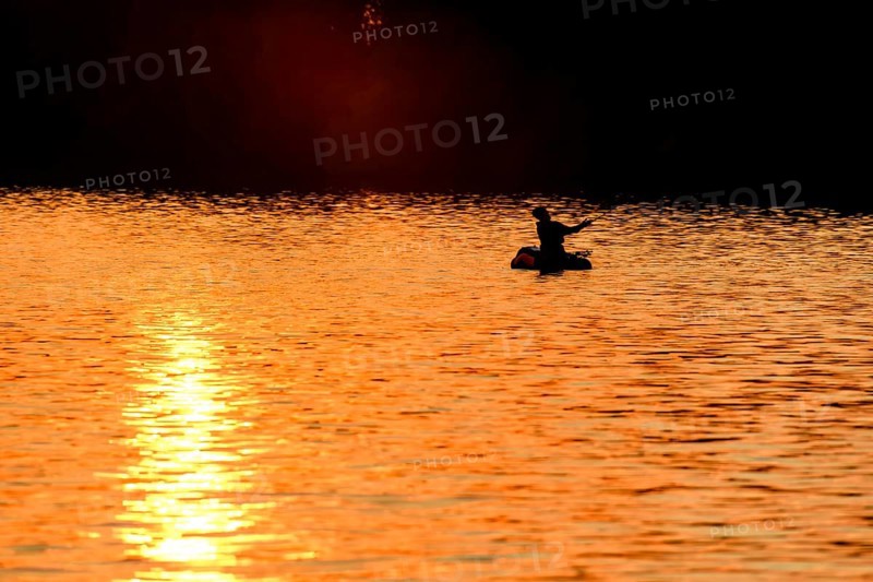 Angler sport fisherman in his belly boat in orange-red lake at sunset, silhouette in calm water, relaxed atmosphere, Lembruch, Dümmer See, Lower Saxony, Germany