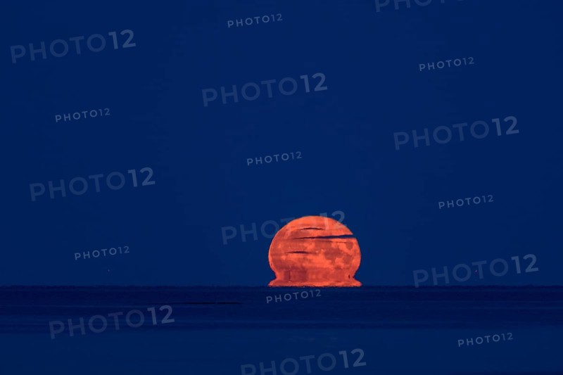 The orange summer moon rises blood-red in darkness over Lake Vänern, blood moon, Värmlandsnäs peninsula, Värmlands län, Sweden