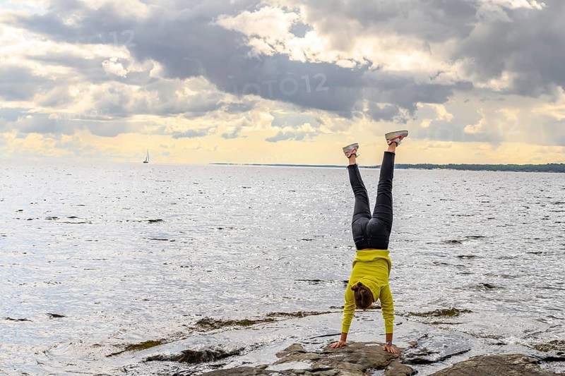 Young woman girl doing a handstand on rocky archipelago at Lake Vänern under cloudy sky, Värmlands län, Sweden