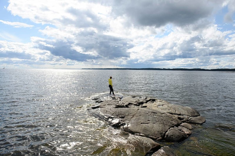 Young woman girl standing on archipelago on rocks at Lake Vänern under cloudy sky, Värmlands län, Sweden