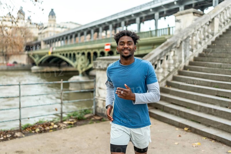 Young athletic man running and smiling at the camera outdoors, exercising along the seine river in paris, finding urban fitness motivation and a healthy lifestyle