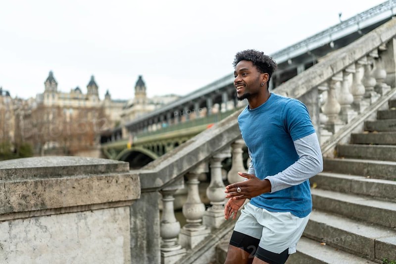 Young black man training and exercising stairs in paris, enjoying fitness and urban lifestyle with a historic bridge and city buildings in the background