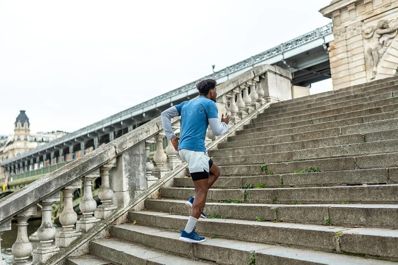 Athletic man training and exercising, running up stone stairs in paris, focusing on fitness and urban sport, with the bir hakeim bridge in the background