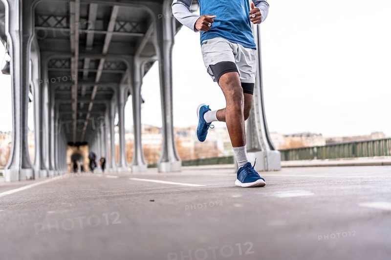 Young man running across a parisian bridge for fitness, showcasing urban training, athletic endurance and active lifestyle amid city architecture and riverbank scenery