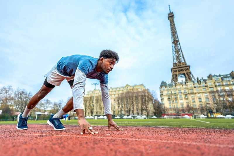 Young male athlete getting ready to run on an outdoor track in the heart of paris, focusing on the starting line with the eiffel tower prominent in the urban background