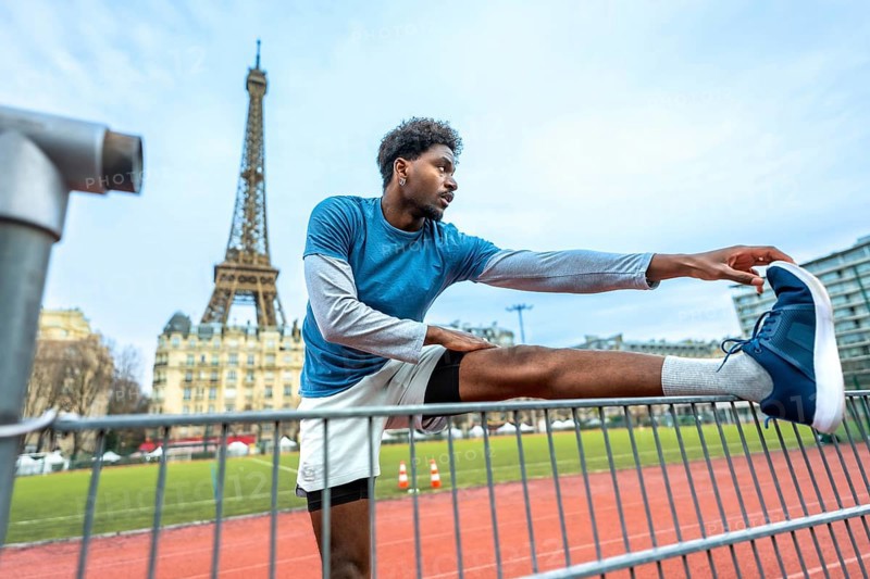 Young athletic man performing stretching exercises on a running track with the iconic eiffel tower in the background, promoting fitness and an active urban lifestyle