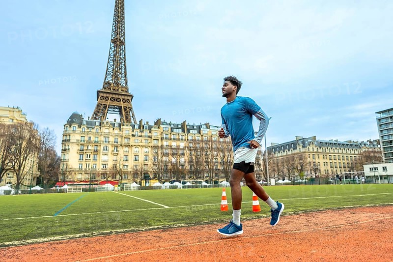 Male athlete running on a sports track in paris, focusing on fitness and active lifestyle in an urban setting with the iconic eiffel tower in the background under a cloudy sky
