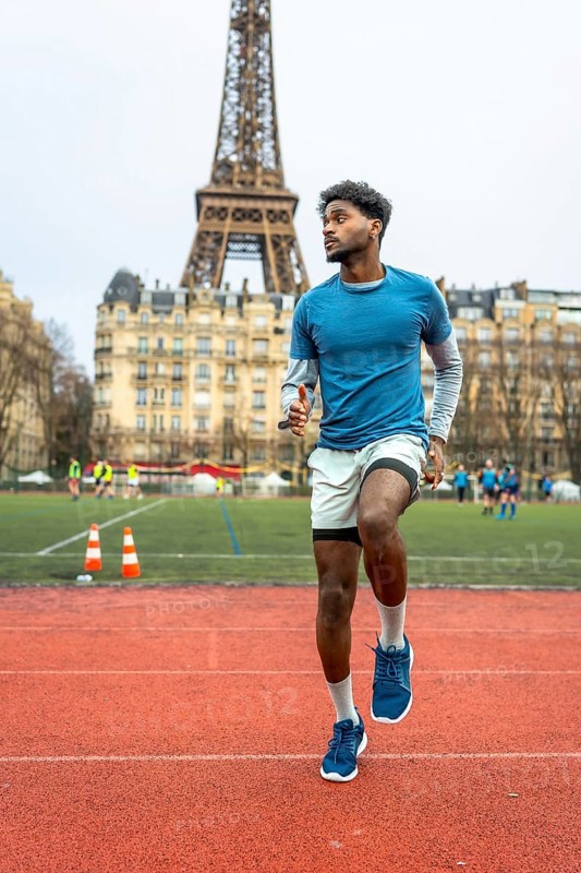 Young man doing speed drills on an outdoor running track, practicing high knees in paris with the iconic eiffel tower and city buildings in the background