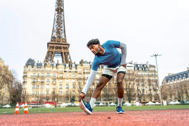 Young black athlete stretching a leg on a running track with the eiffel tower in background, preparing for an urban workout in paris, showcasing fitness and sport in a city environment