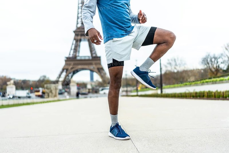 African american male athlete engaging in a high knee exercise or warm up routine, demonstrating fitness and training against the iconic backdrop of the eiffel tower in paris