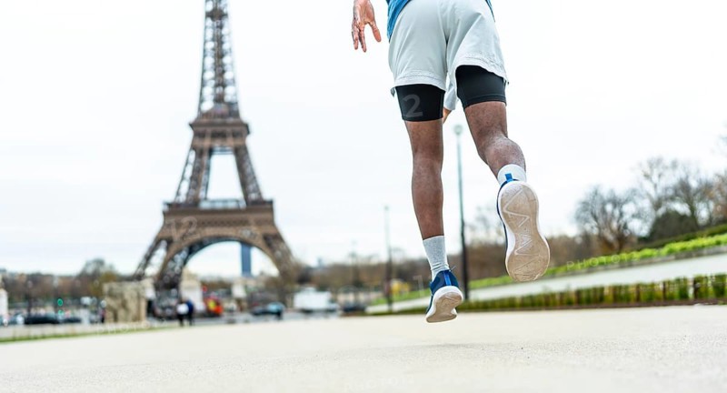 Man running on city street, elevating through a jump or stride, showcasing athleticism and an active urban lifestyle with the iconic parisian landmark in the blurred background