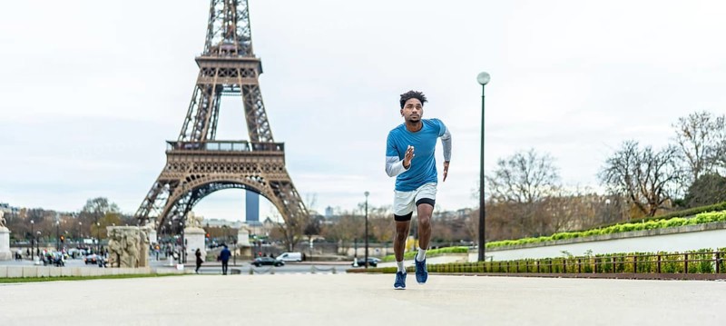Young athletic man jogging through paris streets, focused on training and enjoying an outdoor workout with the blurred eiffel tower and cityscape in the background