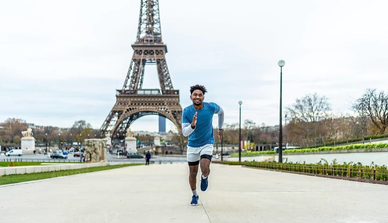 Young man actively running outdoors in front of the eiffel tower, symbolizing fitness, health, and urban sport against the iconic backdrop of the french capital