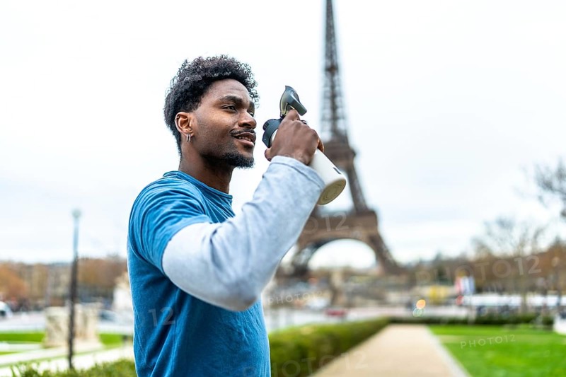Young athletic man hydrating after a workout, holding a water bottle with the eiffel tower in the blurred background, representing urban fitness and a healthy lifestyle in paris