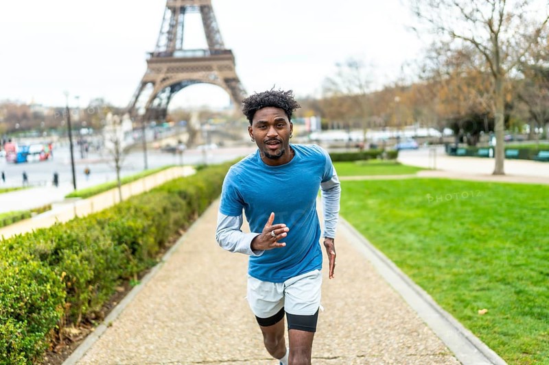 Young black man jogging along a path in a park, maintaining an active lifestyle and fitness routine with the iconic eiffel tower in the background, symbolizing urban health and well being