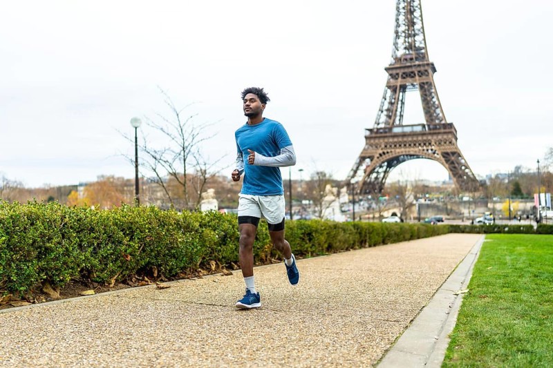 Young man actively jogging along a pathway in a parisian park, focusing on health and fitness with the iconic eiffel tower in the background, representing exercise in a global city